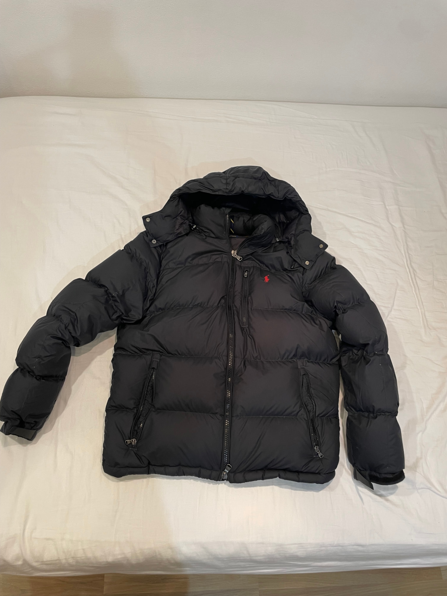 The original phone photo: a black down puffer jacket spread over a white bedsheet in dim room light