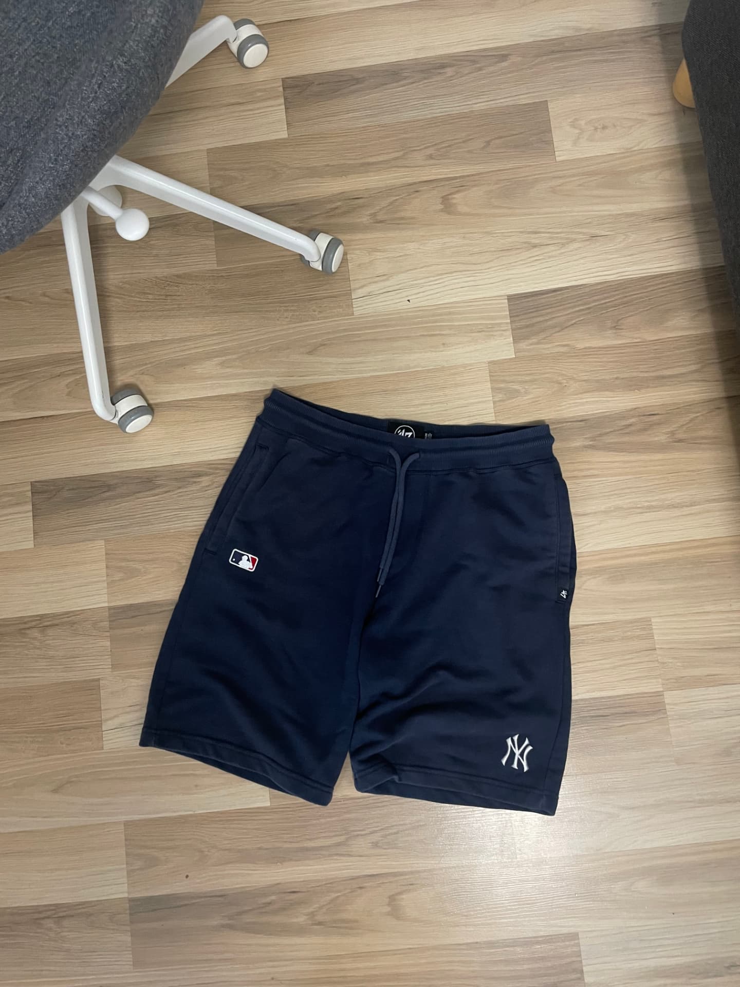 The original phone photo: navy sweat shorts on a wooden floor beside a chair leg, shot at an angle