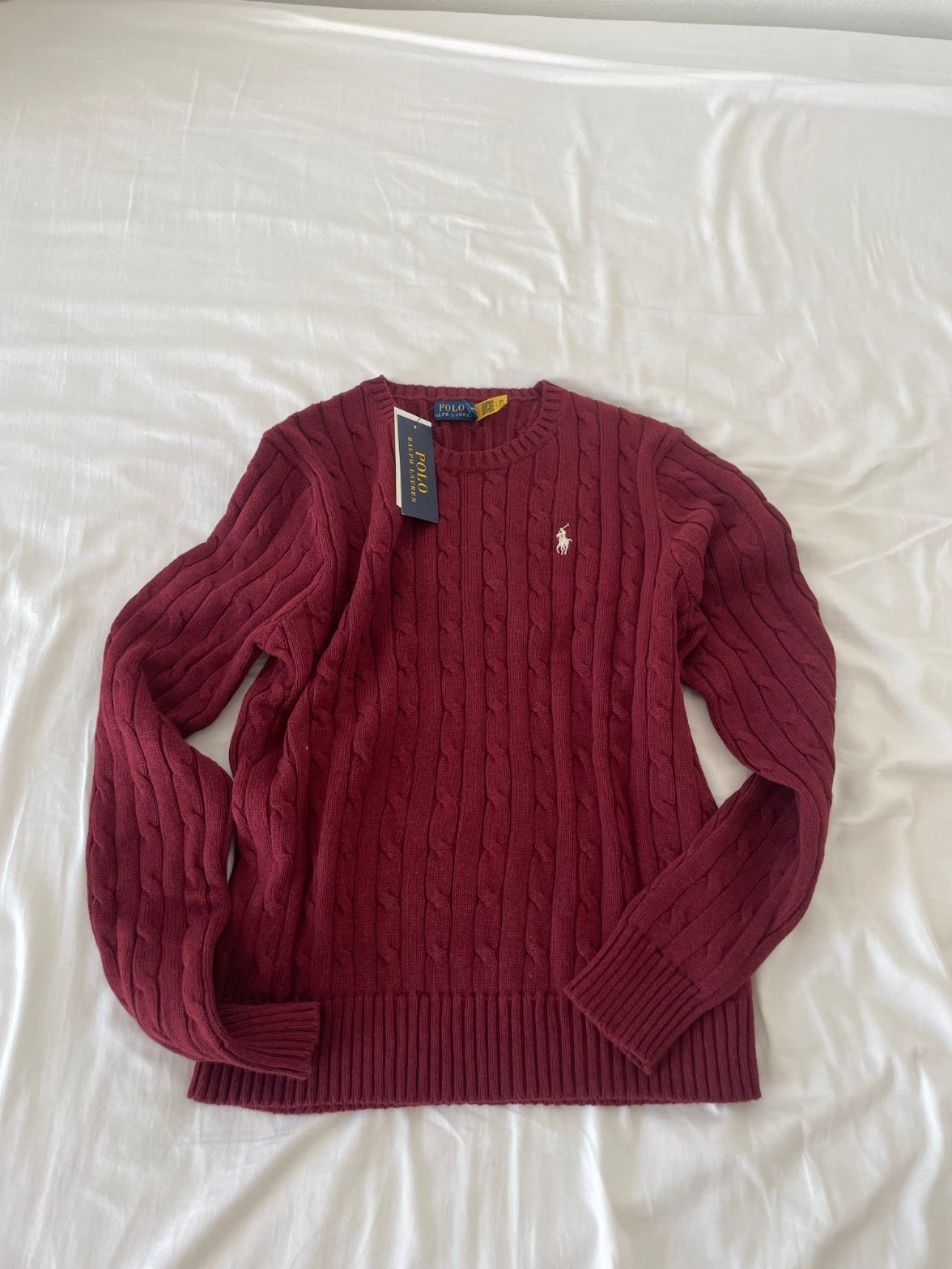 The original phone photo of a burgundy cable-knit Polo Ralph Lauren jumper laid on a white bed
