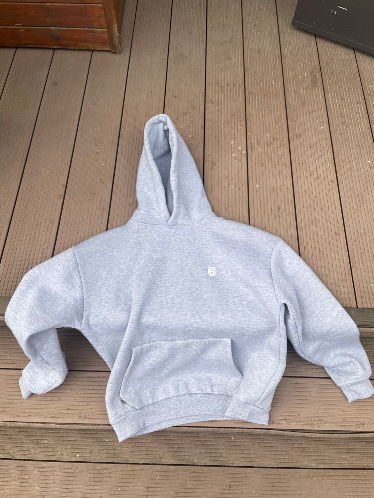 The original phone photo: a grey oversized hoodie lying crumpled on a brown decking board outdoors